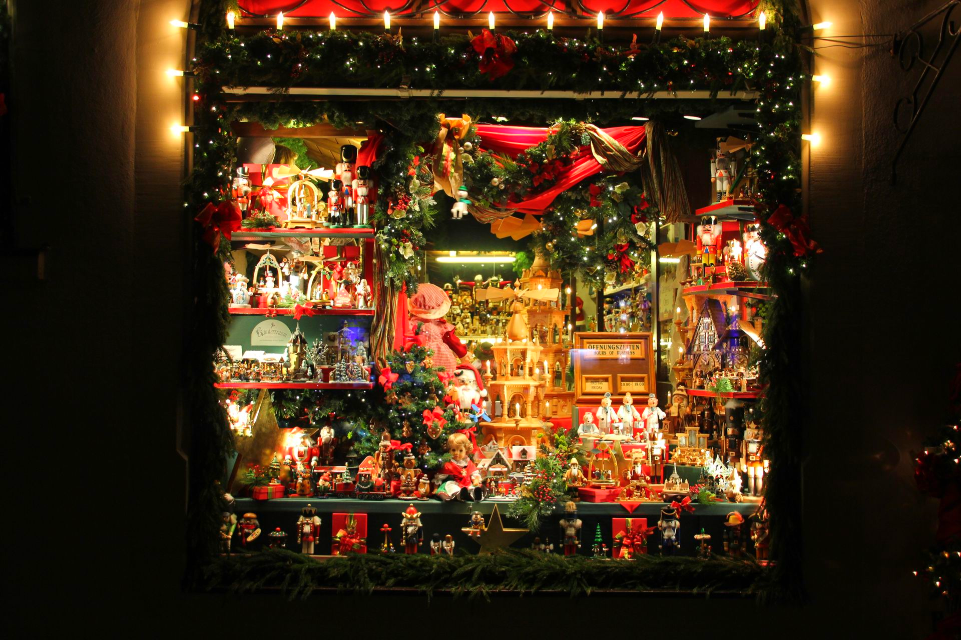 Une vitrine illuminée de guirlandes de Noël, décorée de nombreuses décorations festives, de figurines et de verdure.
