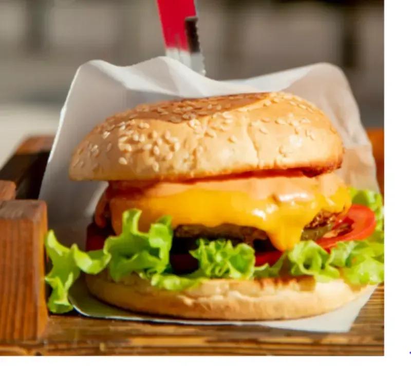 Hamburguesa con queso, lechuga, tomate y queso fundido en un pan de sésamo, servida sobre papel pergamino.
