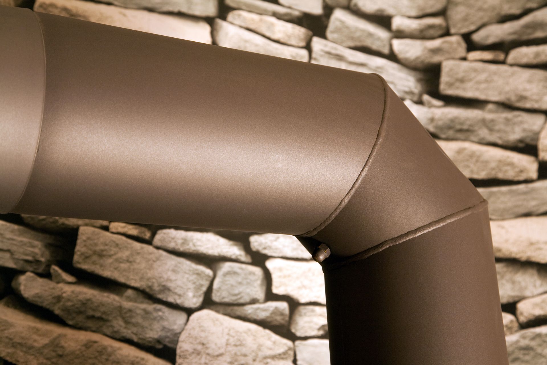Coude de tuyau de poêle marron contre un mur de pierre.