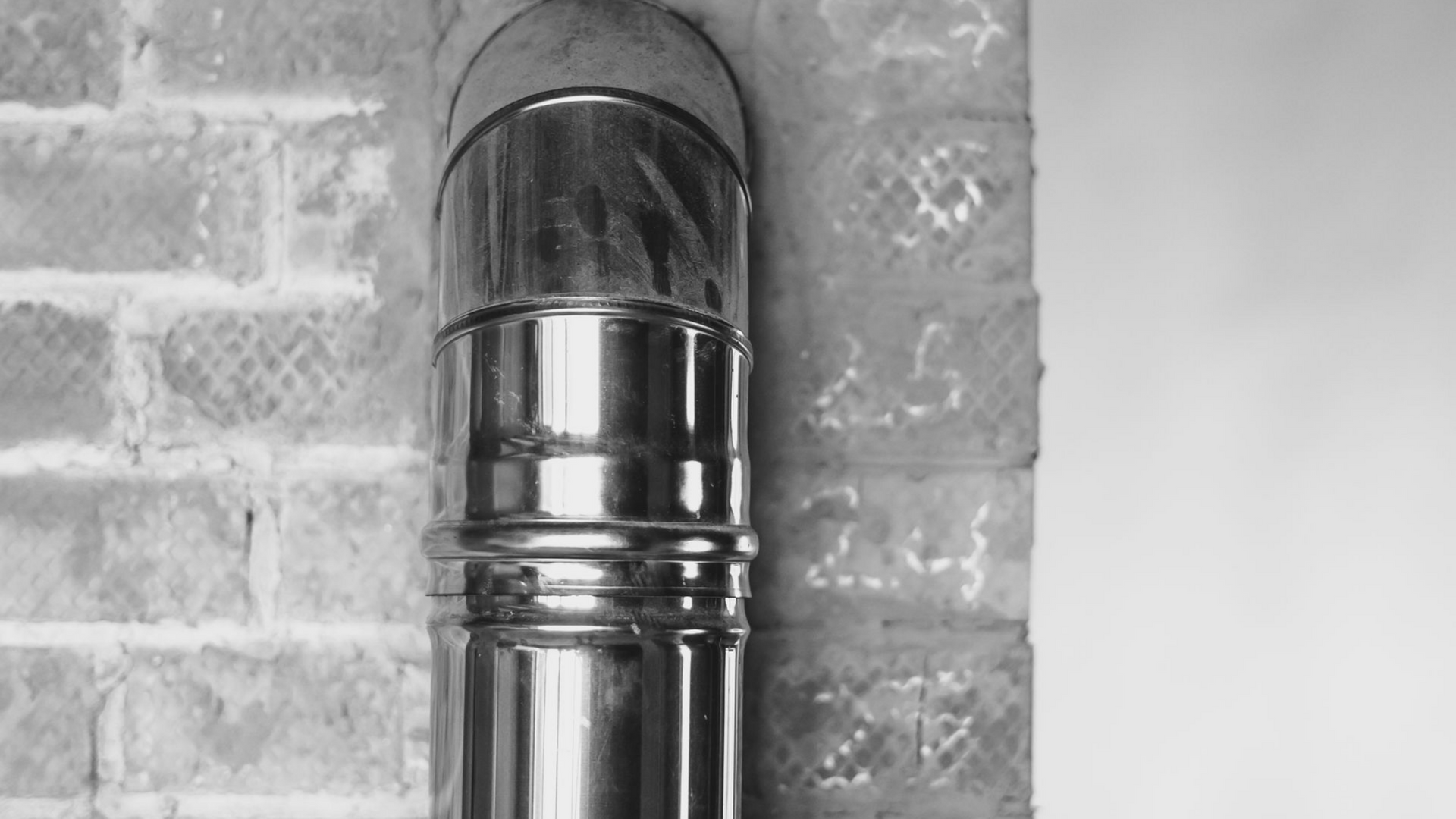 Un tuyau métallique brillant est fixé sur un mur de briques.