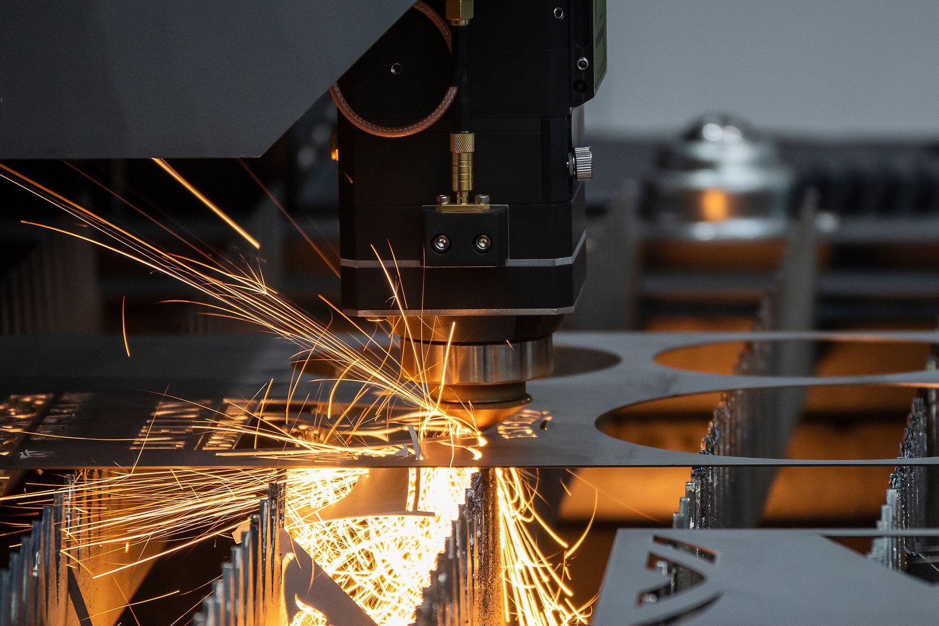Machine de découpe laser, des étincelles jaillissent tandis qu'elle découpe des formes dans une tôle.