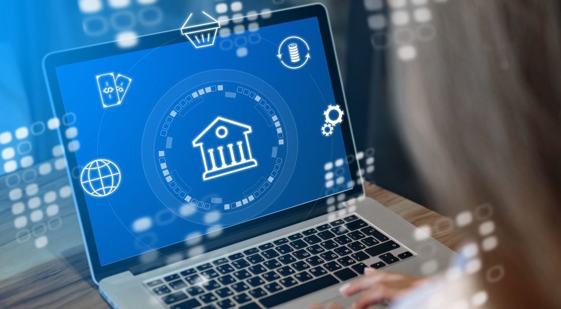 Persona que utiliza una computadora portátil, pantalla de banca en línea con ícono de banco y símbolos financieros.