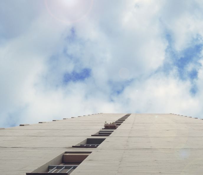 Mirando hacia arriba a un edificio alto y blanco con filas de ventanas contra un cielo nublado.