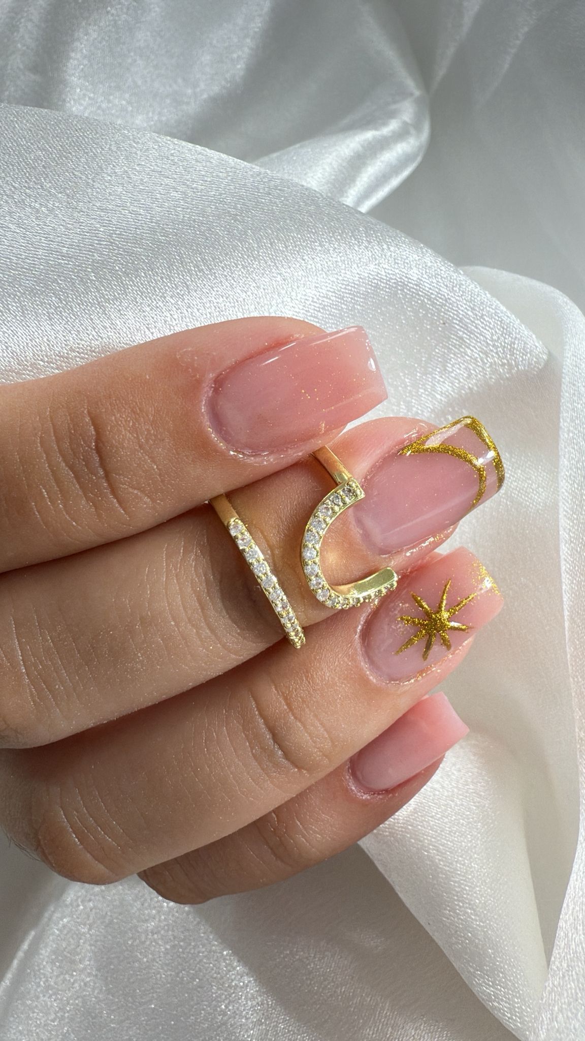 Mano con uñas manicuradas y anillos; un anillo en forma de V con diamantes y un anillo recto en un dedo.