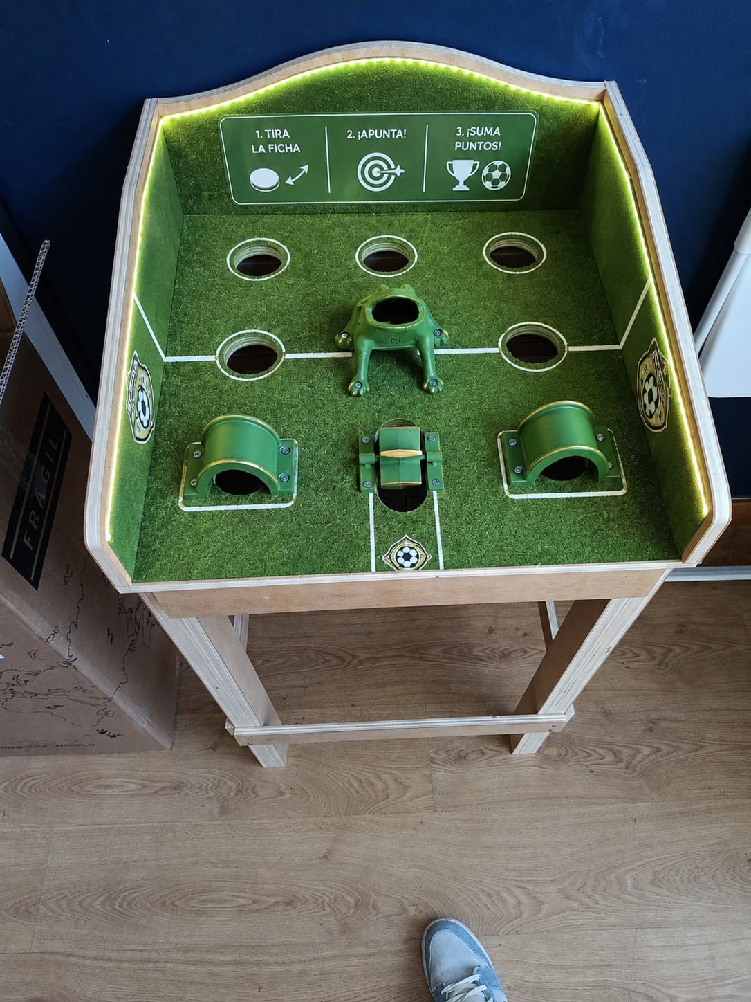 Tablero de juego de mesa verde con agujeros y rampas sobre un soporte pequeño, visto desde arriba