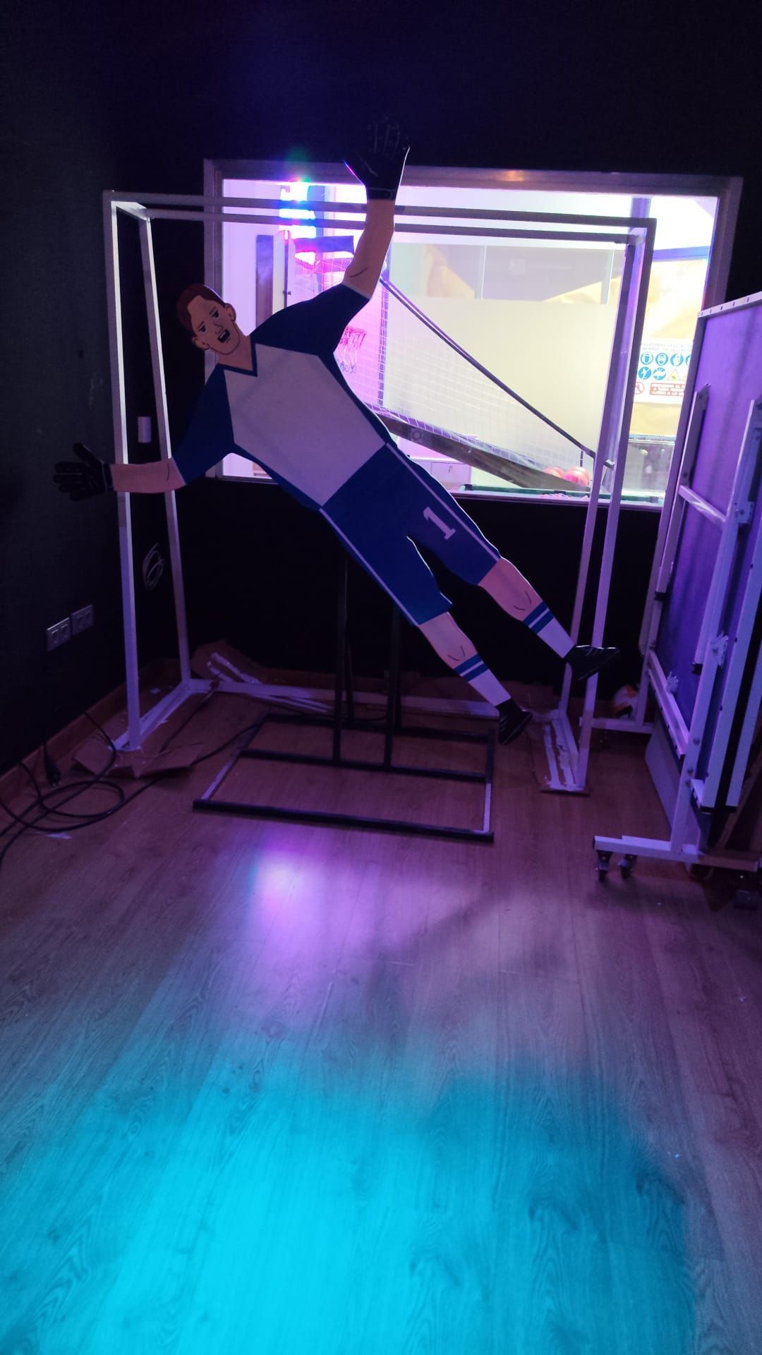 Una persona inclinada hacia un lado dentro de un gran marco transparente en una habitación iluminada de color morado.