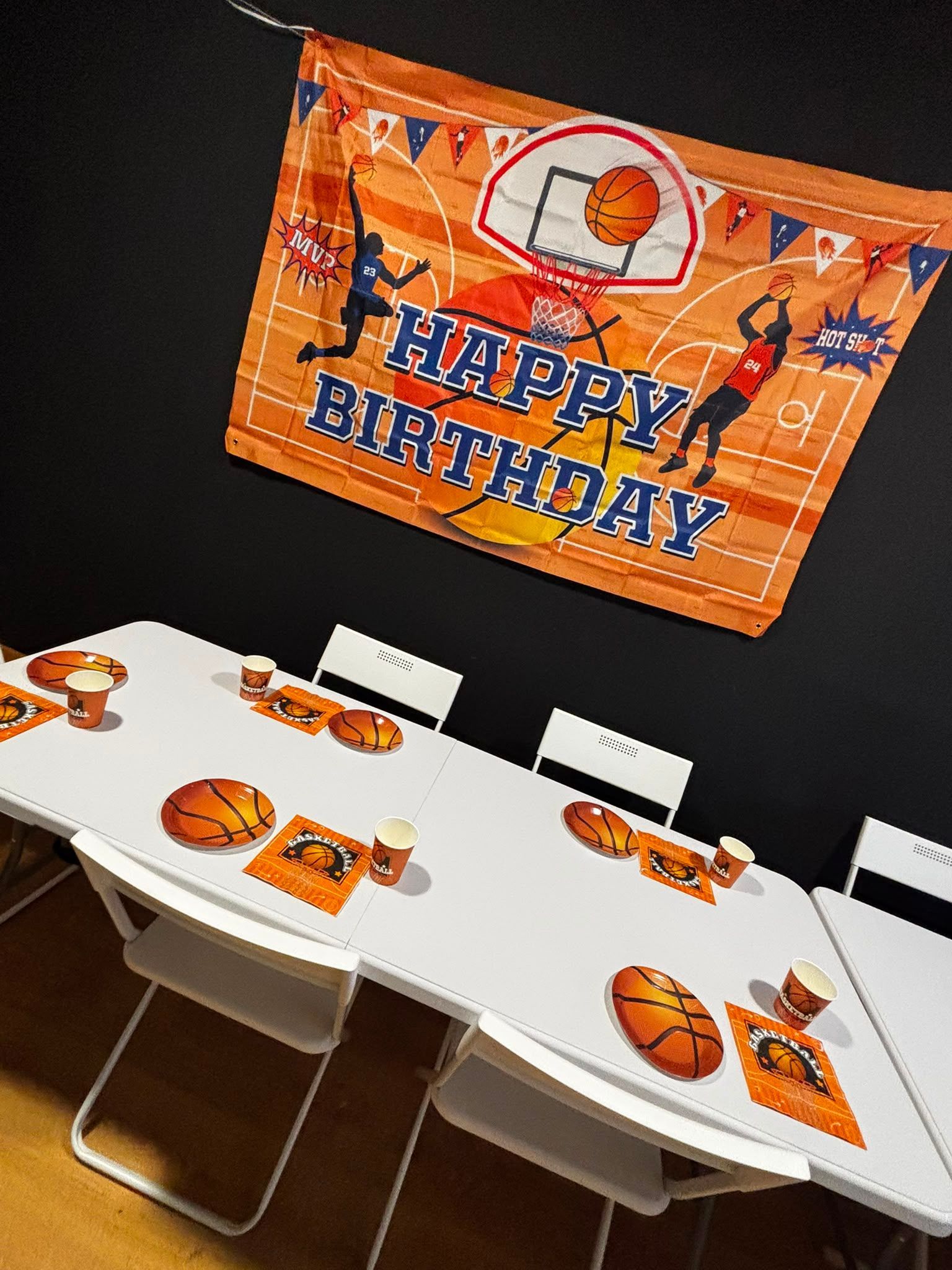 Mesa de cumpleaños decorada con adornos naranjas y una pancarta de «Feliz cumpleaños» en una pared negra