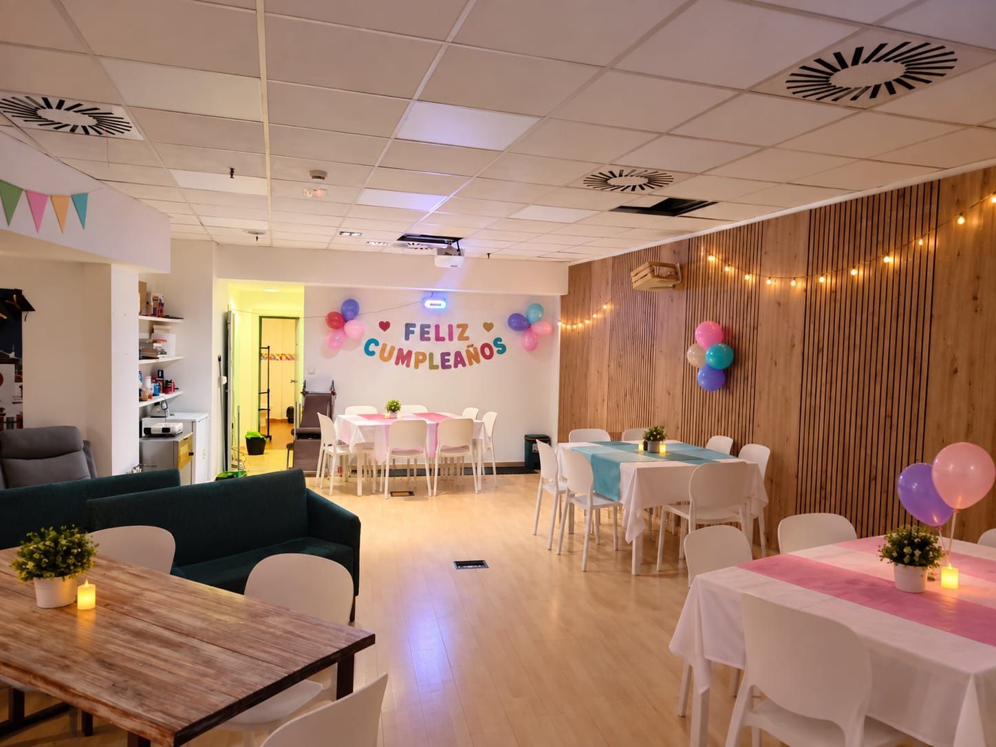 Montaje de fiesta de cumpleaños en una sala decorada con mesas, globos, guirnaldas de luces y una pancarta que dice “FELIZ CUMPLEAÑOS”