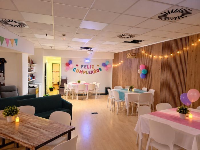 Montaje de fiesta de cumpleaños en una sala decorada con mesas, globos, guirnaldas de luces y una pancarta que dice “FELIZ CUMPLEAÑOS”