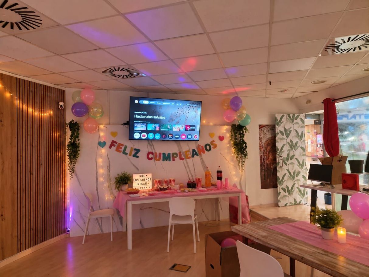 Preparativos para una fiesta de cumpleaños con una mesa rosa, globos, una pancarta, un televisor y luces cálidas en guirnalda