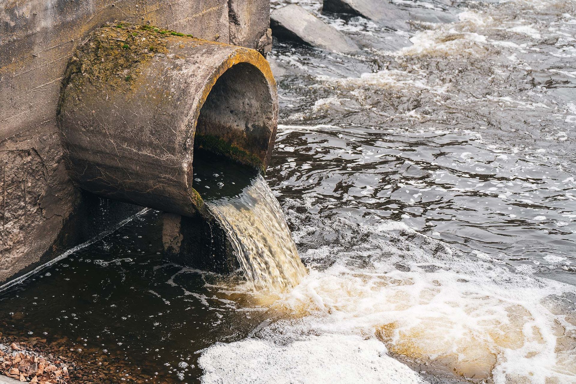 Durch ein Rohr wird Wasser in einen Fluss abgeleitet.