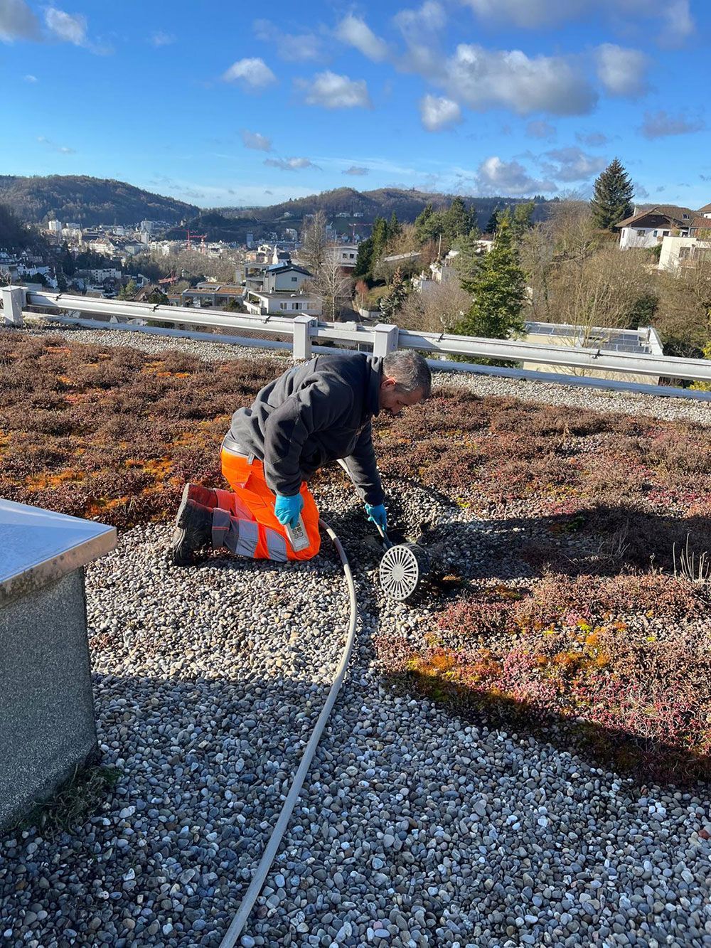 Ein Mann kniet mit einem Schlauch auf einem Kiesdach.