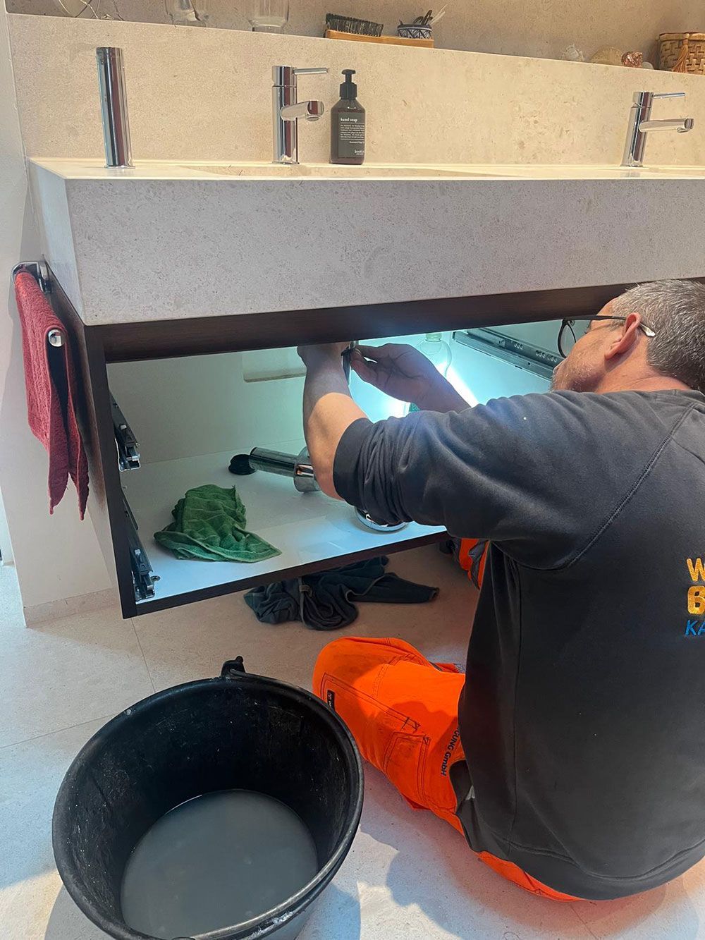 Ein Mann kniet auf dem Boden und repariert ein Waschbecken in einem Badezimmer.