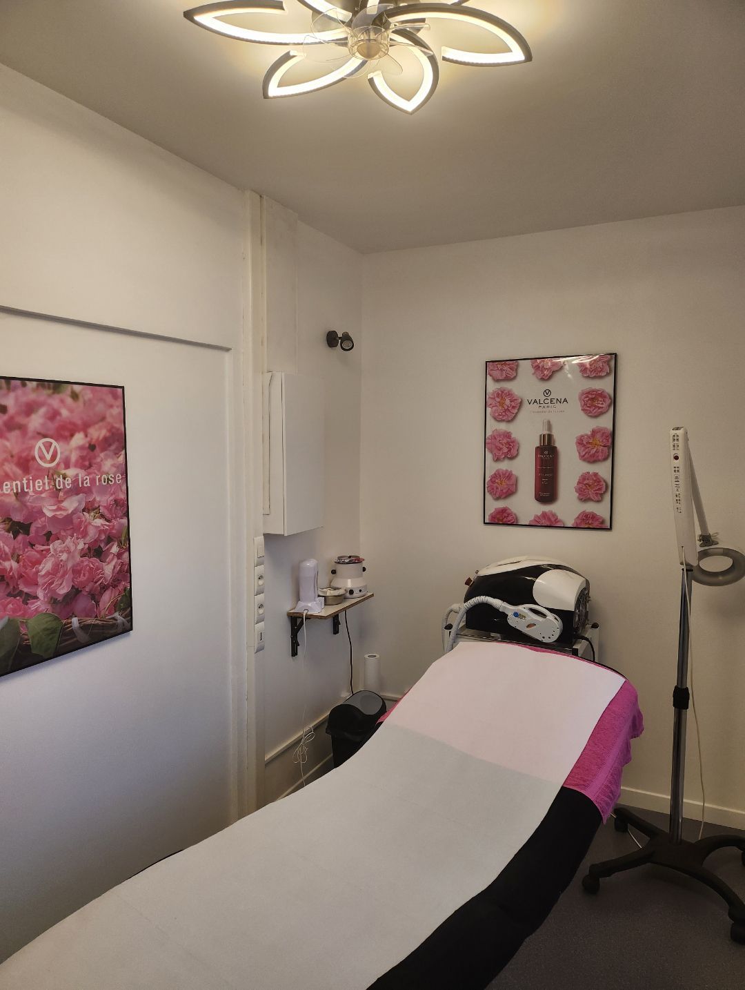 Table de massage dans une pièce blanche avec lustre au plafond et des appareils pour des soins de beautés.