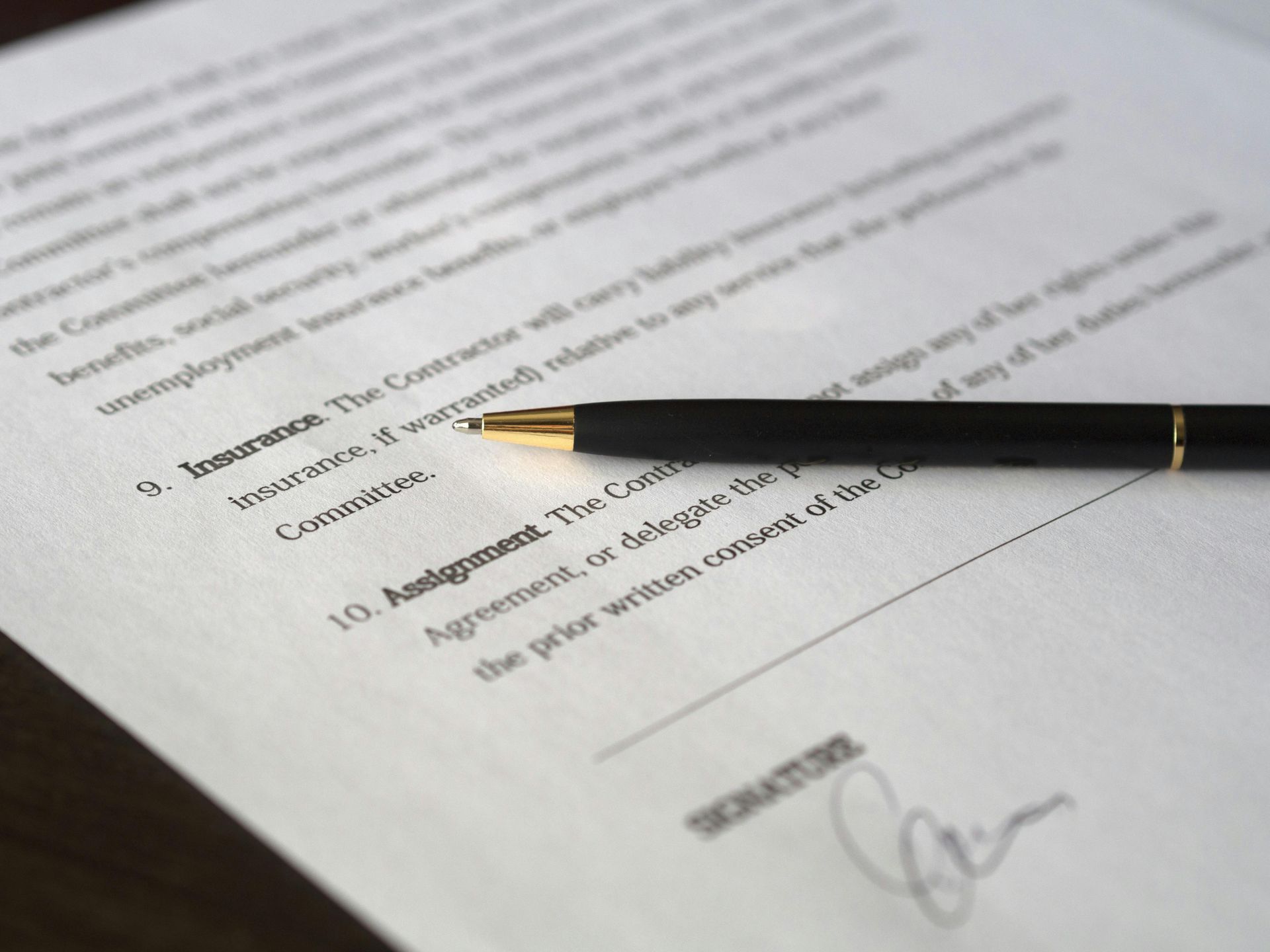 Un bolígrafo reposa sobre un contrato con texto, resaltando secciones sobre seguro y cesión, listo para firmar.