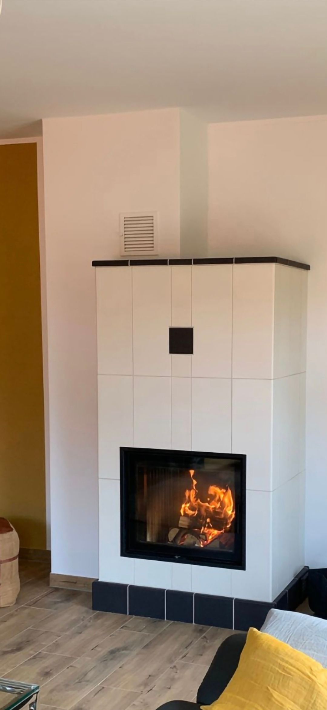 Weiß gefliester Kamin mit brennendem Feuer im Inneren.