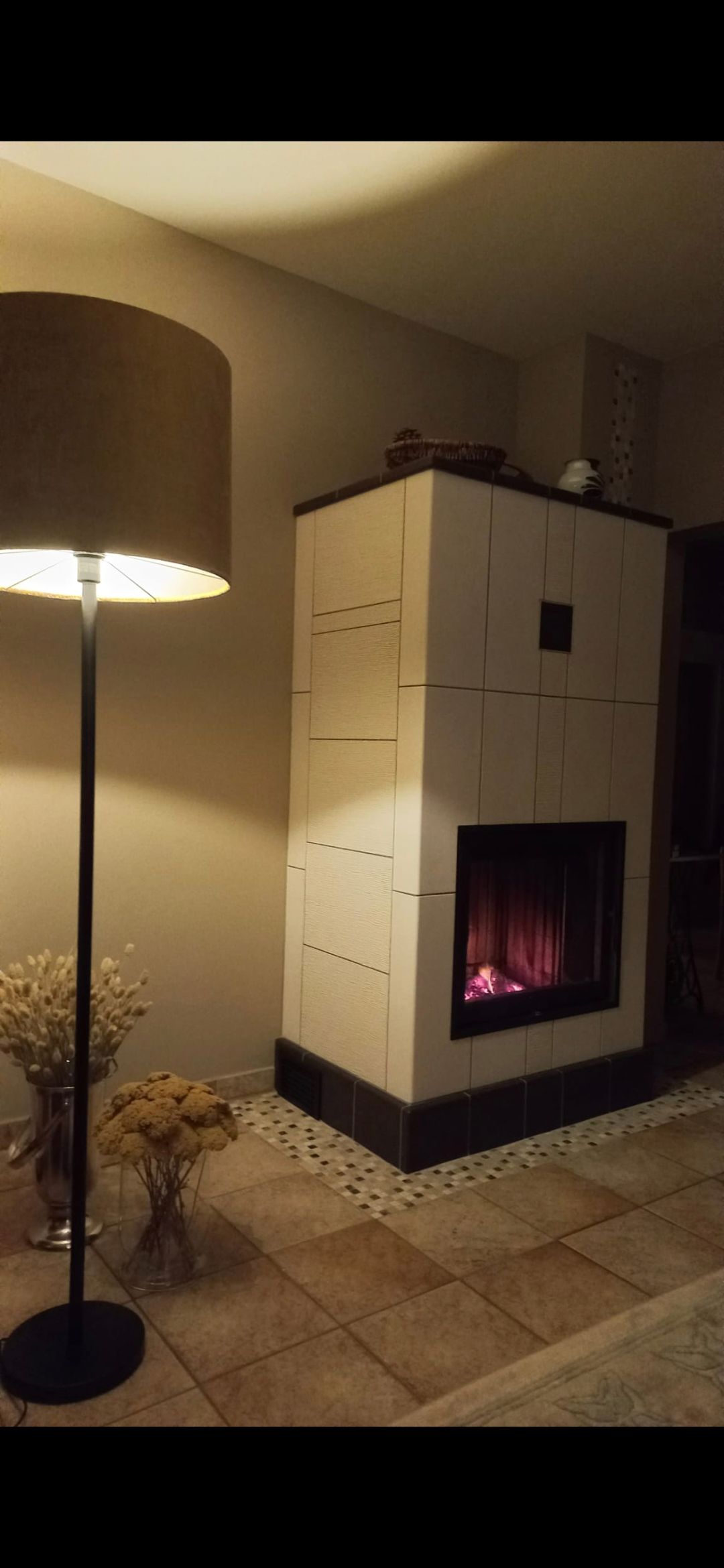 Ein brennender Kamin und eine Stehlampe in einem Raum mit Fliesenboden.