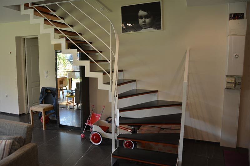 Un escalier moderne avec des rampes en métal blanc et des marches en bois foncé, à l'intérieur d'un espace de vie lumineux.