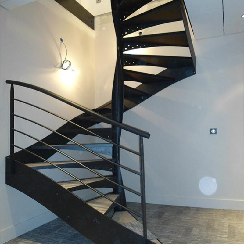 Un escalier en colimaçon noir avec une rampe en métal contre un mur blanc dans une pièce au sol clair.