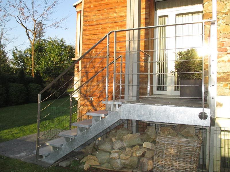 Un escalier extérieur en métal avec une rampe mène à une porte d'entrée d'une maison en briques, avec un tas de pierres en dessous.