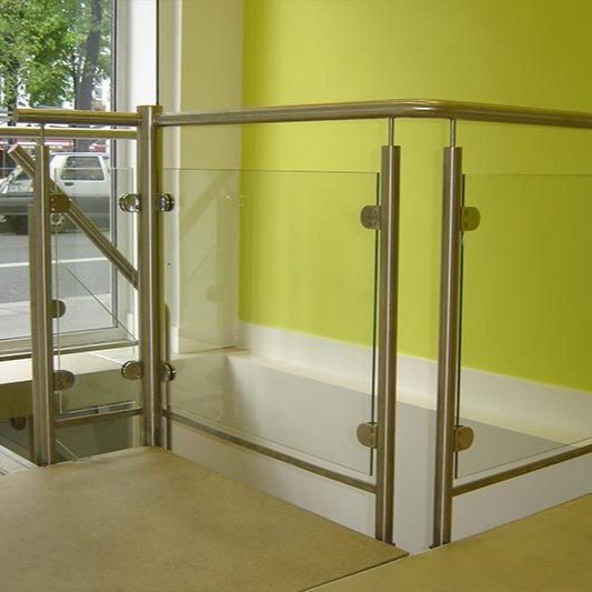 Une rampe d'escalier moderne avec des poteaux en acier inoxydable, des fixations circulaires en verre et des panneaux de verre transparent contre un mur en chaux.