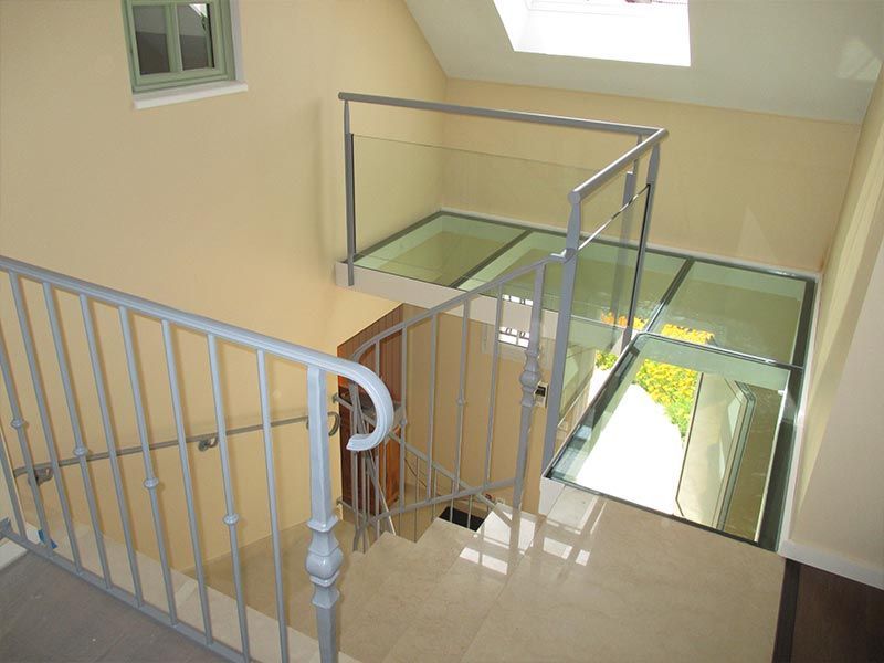 Un escalier avec une rampe métallique menant à un palier dont le plancher est recouvert de panneaux de verre donnant sur l'étage inférieur.