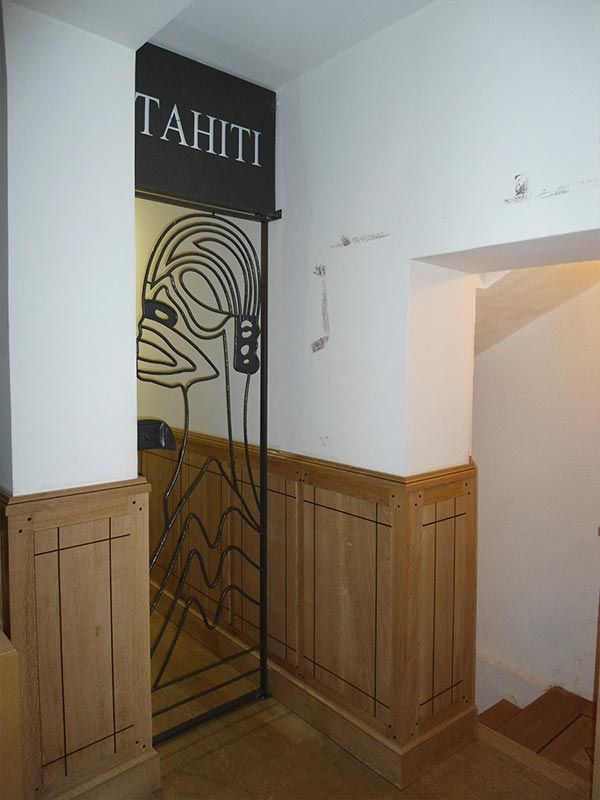 Une porte ornée d'une grille métallique représentant un visage dessiné au trait et le mot « TAHITI », dans une pièce aux boiseries claires.