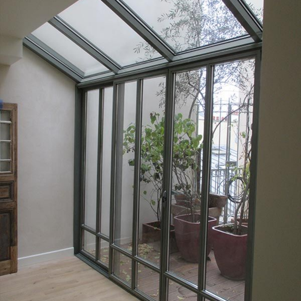 Une véranda avec un plafond en pente vitré et de grandes portes coulissantes donnant sur une petite terrasse avec des plantes en pot.