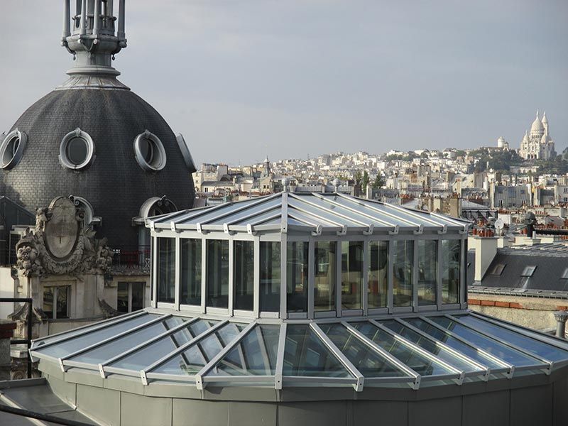À Paris, un atrium vitré jouxte le toit en dôme d'un immeuble, avec la basilique du Sacré-Cœur en arrière-plan.