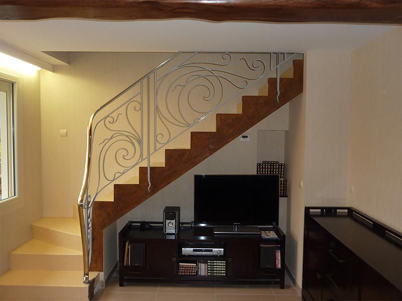 Un téléviseur et un meuble multimédia sont placés sous un escalier en bois avec une rampe en métal décoratif dans un espace de vie.