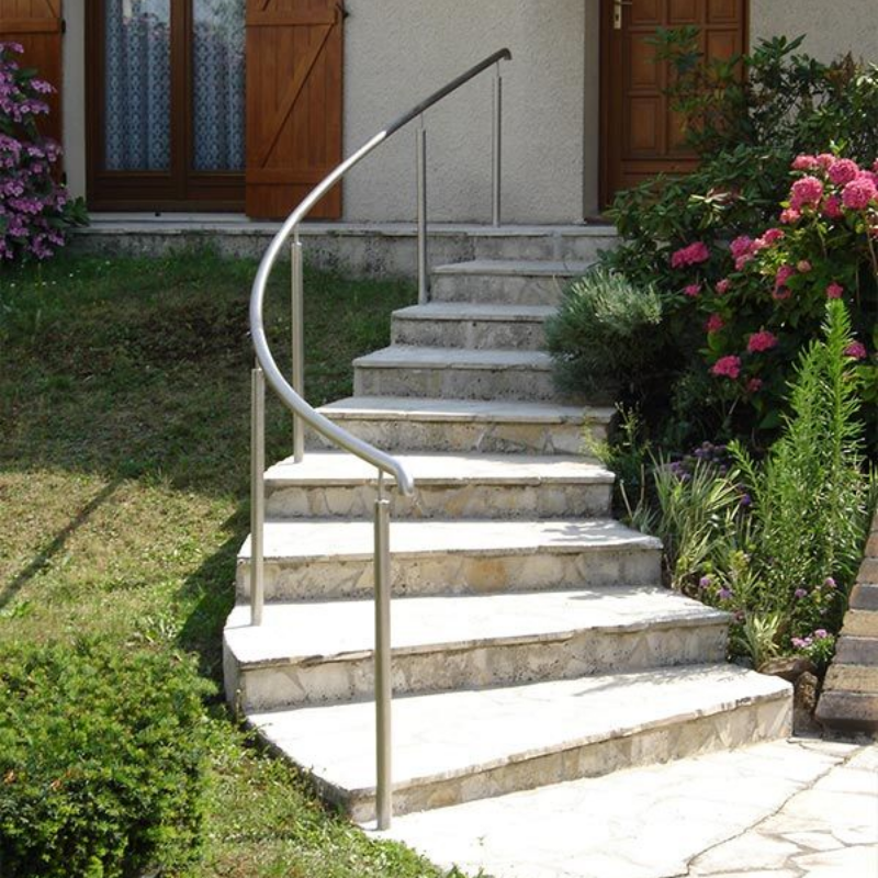 Escalier extérieur en pierre incurvé menant à l'entrée de la maison, avec une rampe métallique moderne sur la gauche.