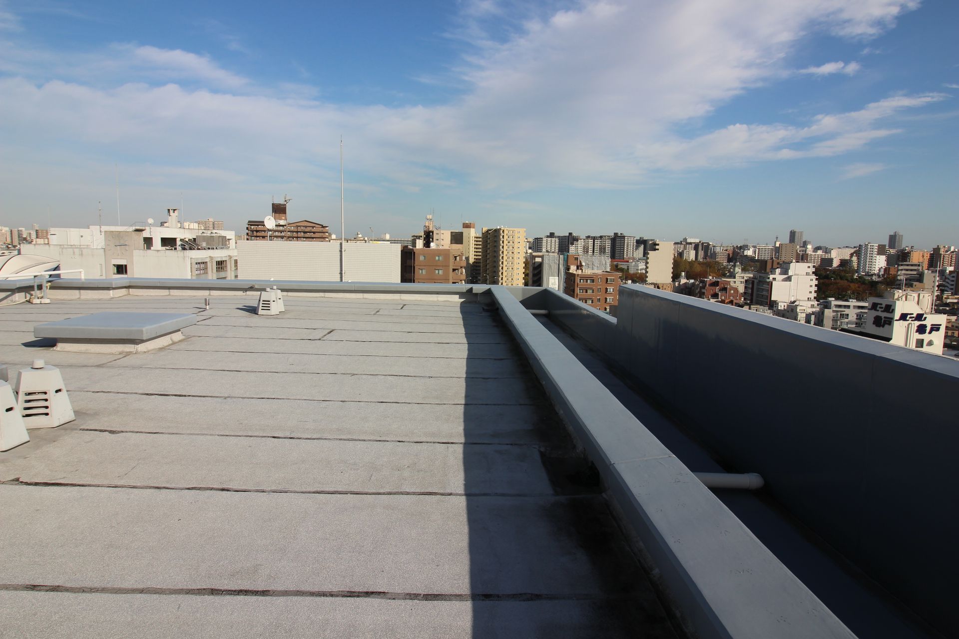Toit-terrasse avec un parapet bas surplombant une dense ligne d'horizon urbaine sous un ciel bleu clair.