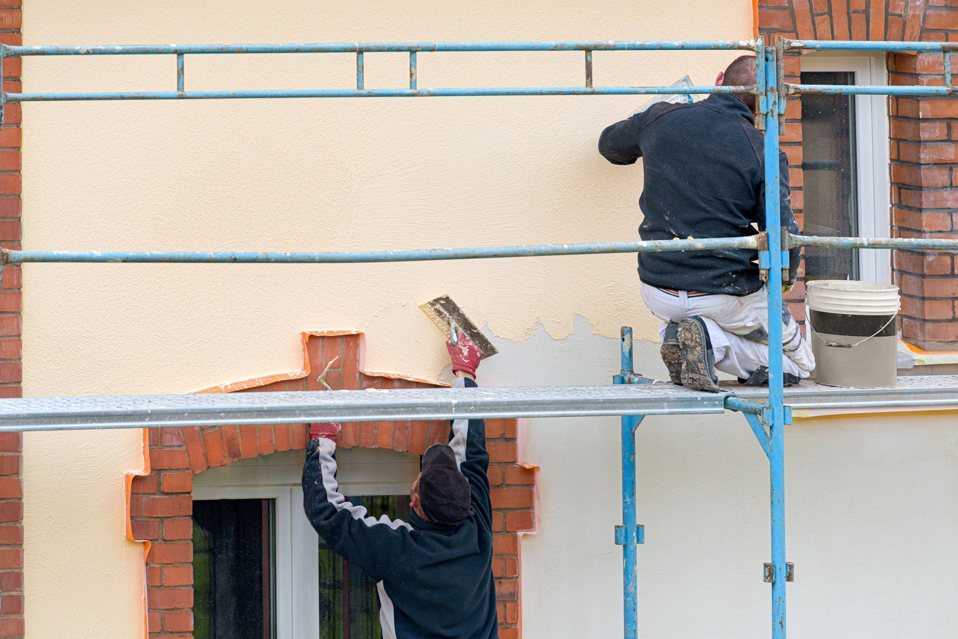 Deux ouvriers sur un échafaudage peignent l'extérieur beige d'un bâtiment.