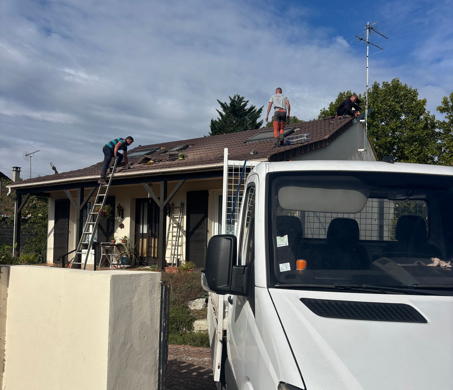 Des ouvriers travaillent sur le toit d'une maison à côté d'un camion blanc dans une cour résidentielle.