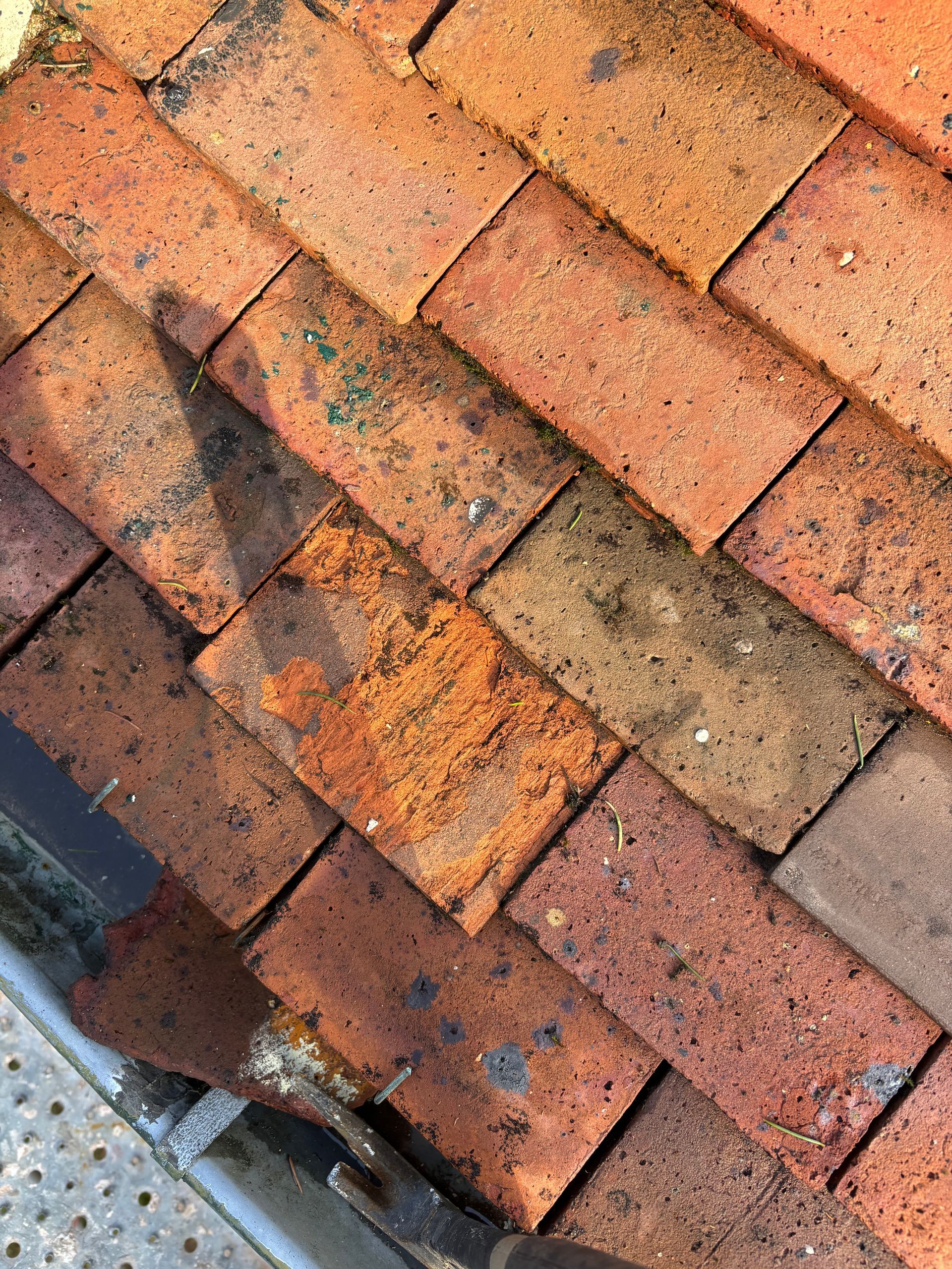 Gros plan sur des tuiles de toit en terre cuite rouges patinées, présentant des taches sombres.