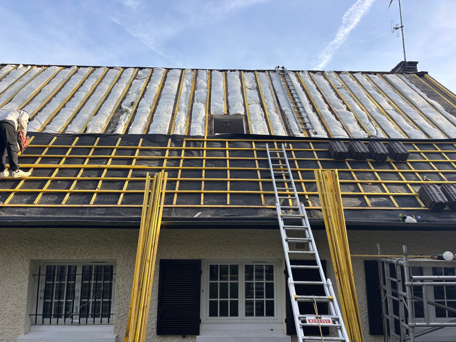 Réparation du toit d'une maison extérieure à l'aide d'échafaudages et d'échelles jaunes.