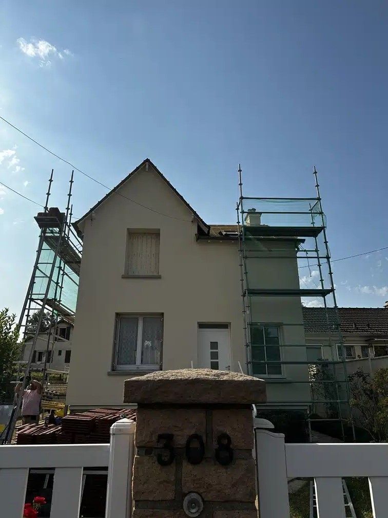 Maison en construction avec des échafaudages de chaque côté et un ciel bleu clair au-dessus.