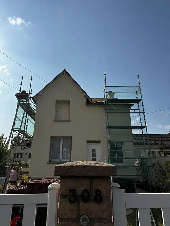 Maison entourée d'échafaudages des deux côtés sous un ciel bleu azur.