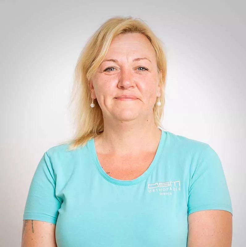 Eine Frau mit blauem T-Shirt und Ohrringen lächelt in die Kamera.