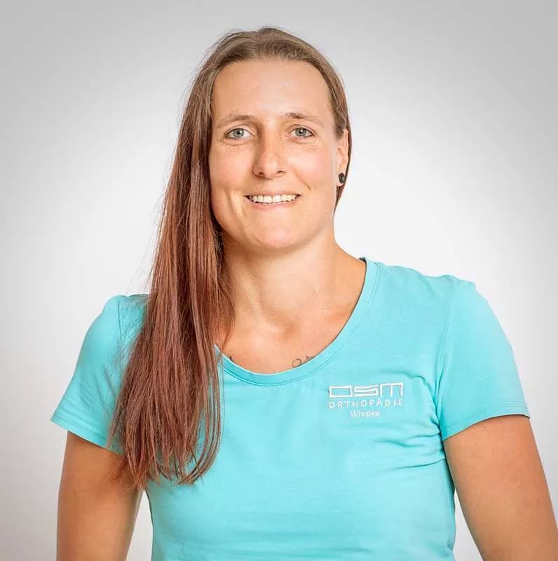 Eine Frau mit langen Haaren trägt ein blaues T-Shirt und lächelt.