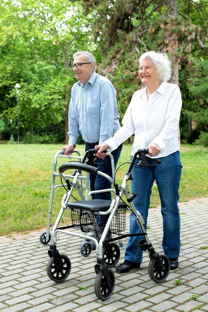 Ein älteres Ehepaar geht mit einer Gehhilfe einen Bürgersteig entlang.