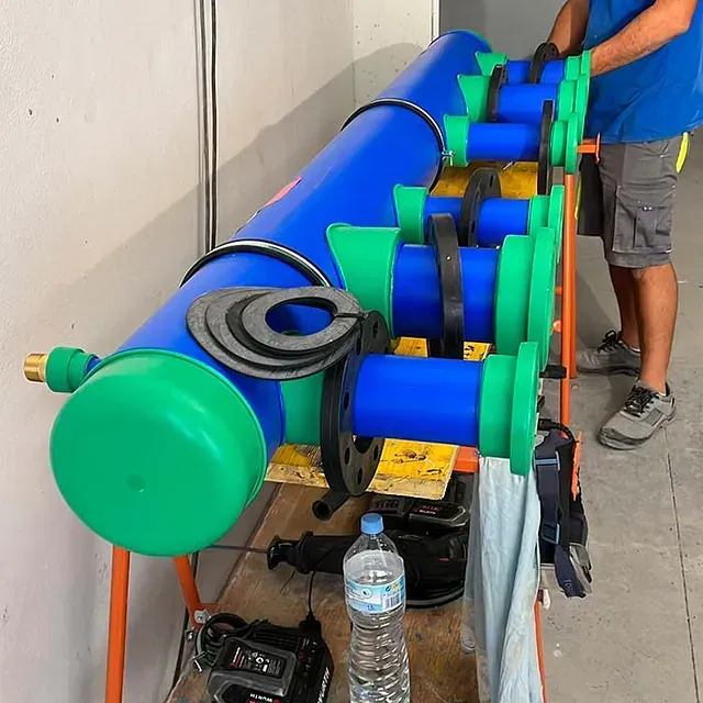 Un hombre está de pie junto a una fila de tubos azules y verdes.