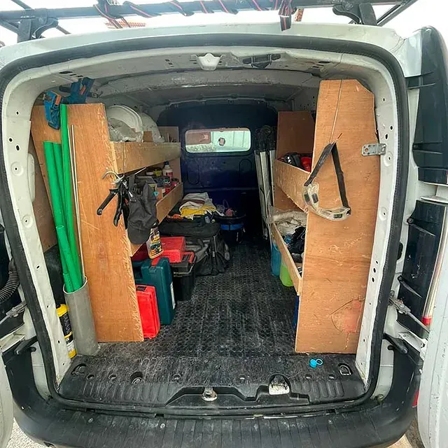 La parte trasera de una furgoneta blanca con estantes de madera y un portaequipajes en el techo.