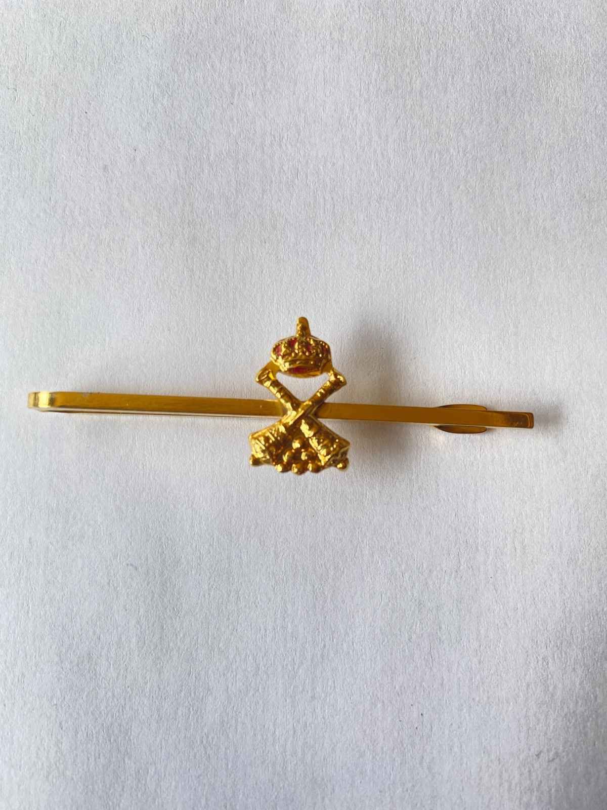 Horquilla decorativa de tono dorado con un pequeño adorno floral central sobre fondo blanco.