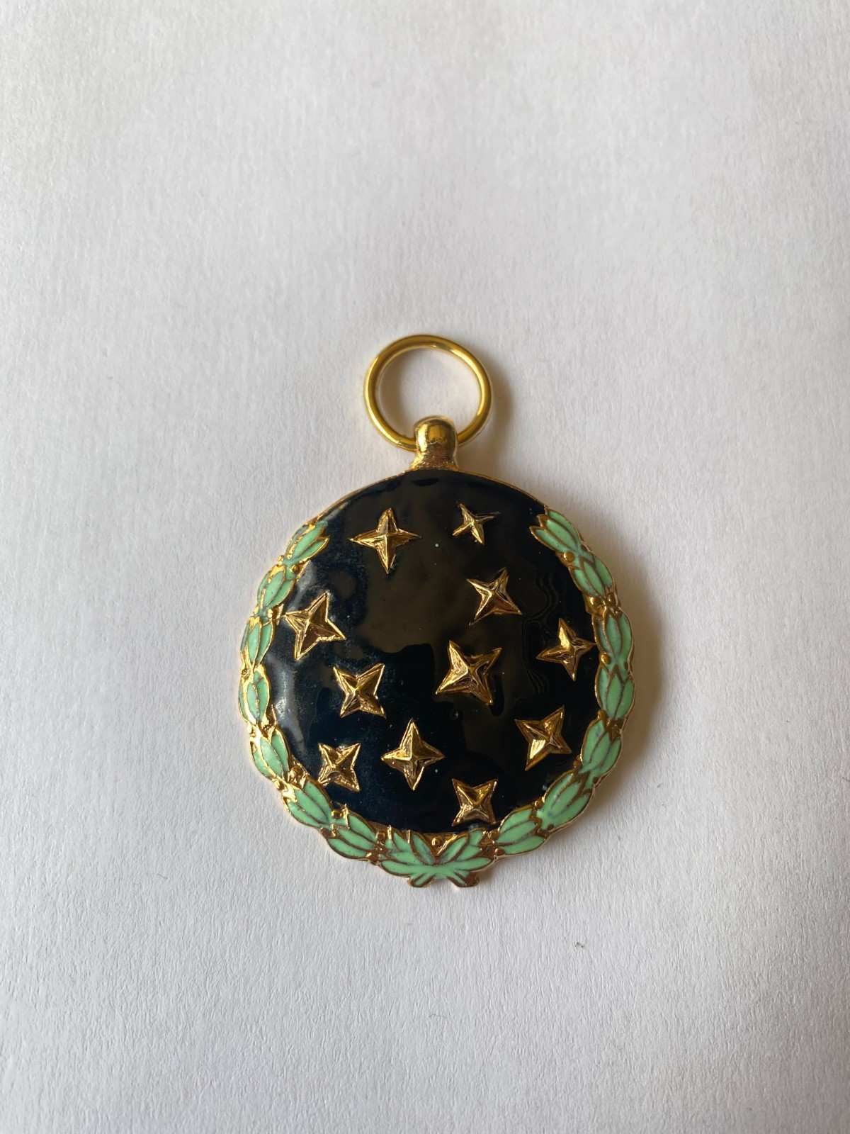 Colgante dorado y negro con estampado de estrellas y borde verde sobre fondo blanco.
