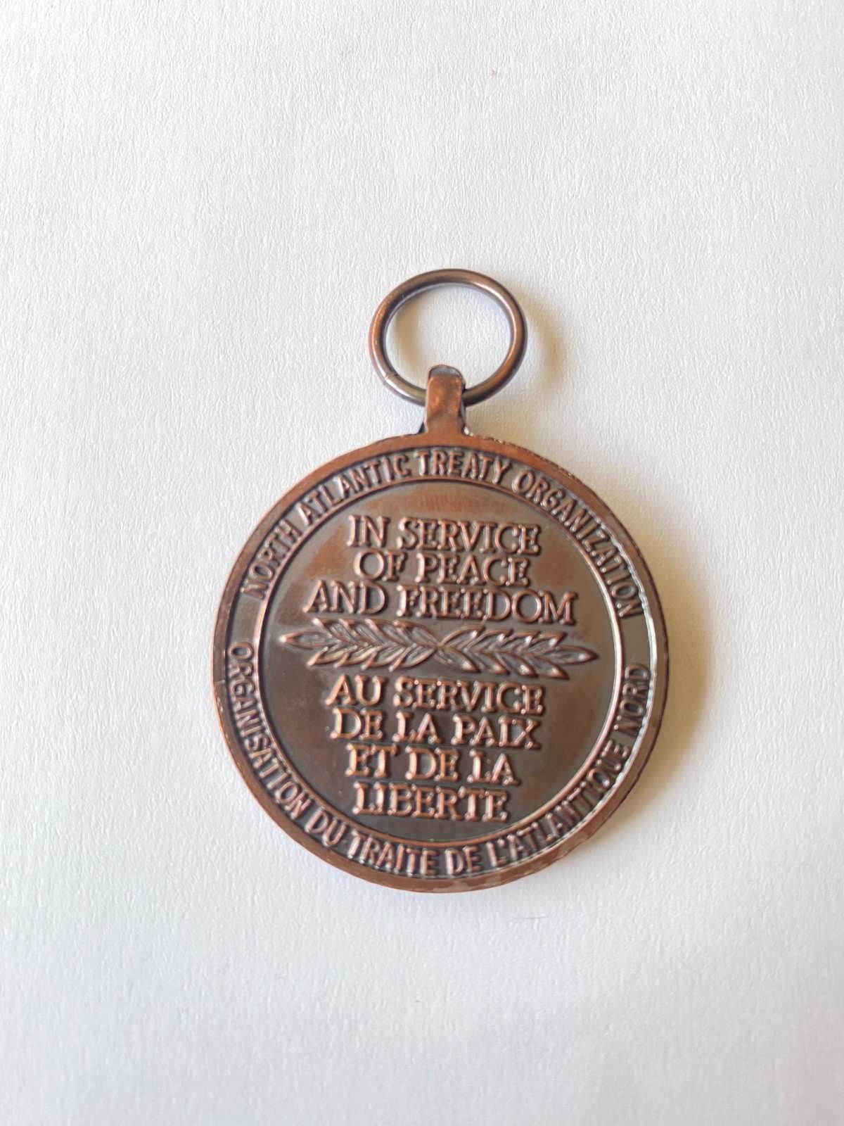 Primer plano de una medalla conmemorativa de bronce con una argolla, que muestra texto grabado sobre un fondo blanco.