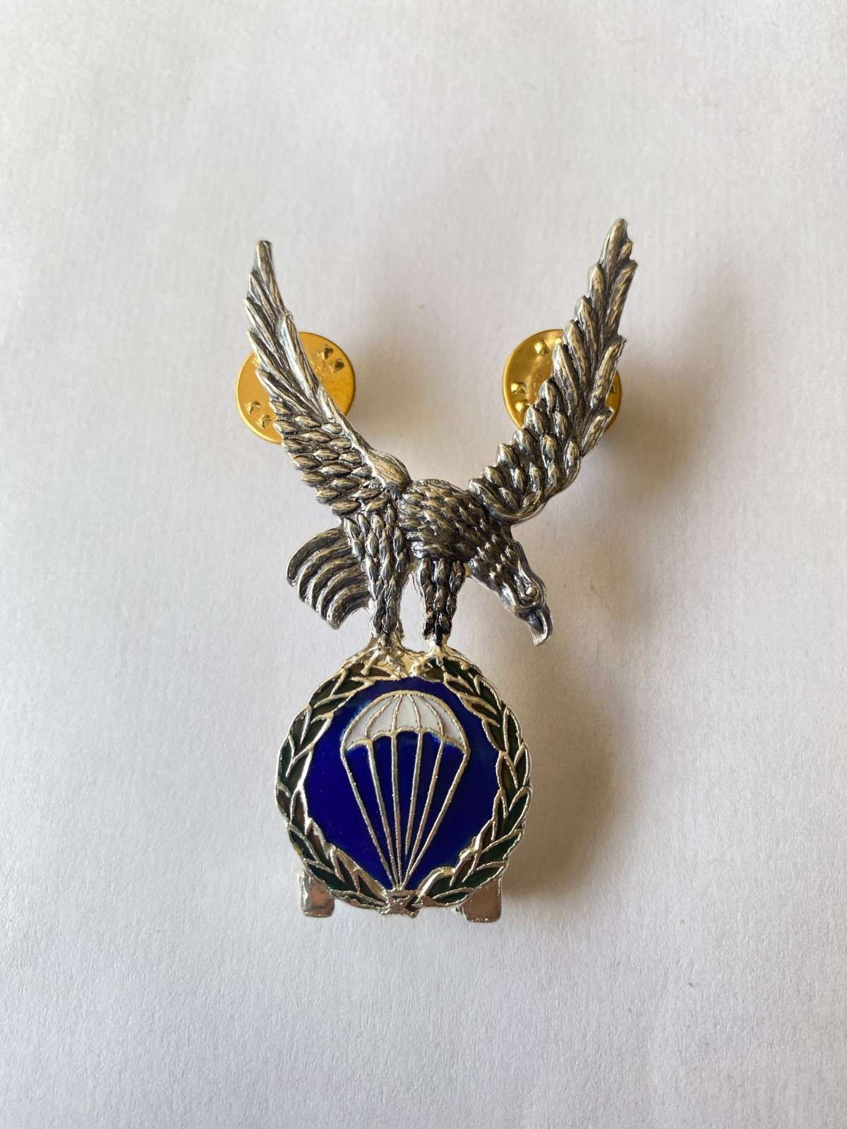 Insignia del águila plateada con emblema de paracaídas azul sobre fondo blanco.