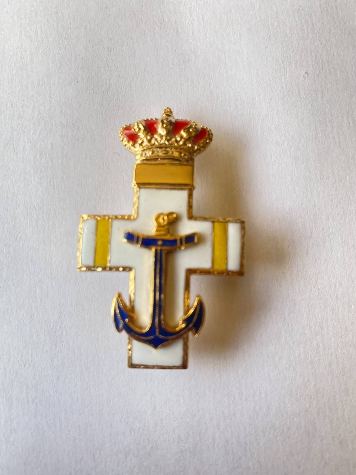 Broche de cruz con ancla dorada y azul con una corona sobre fondo blanco