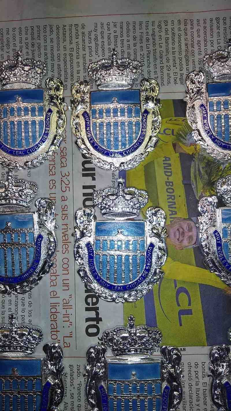 Pines azules y plateados con forma de escudo dispuestos en filas sobre un envase impreso.