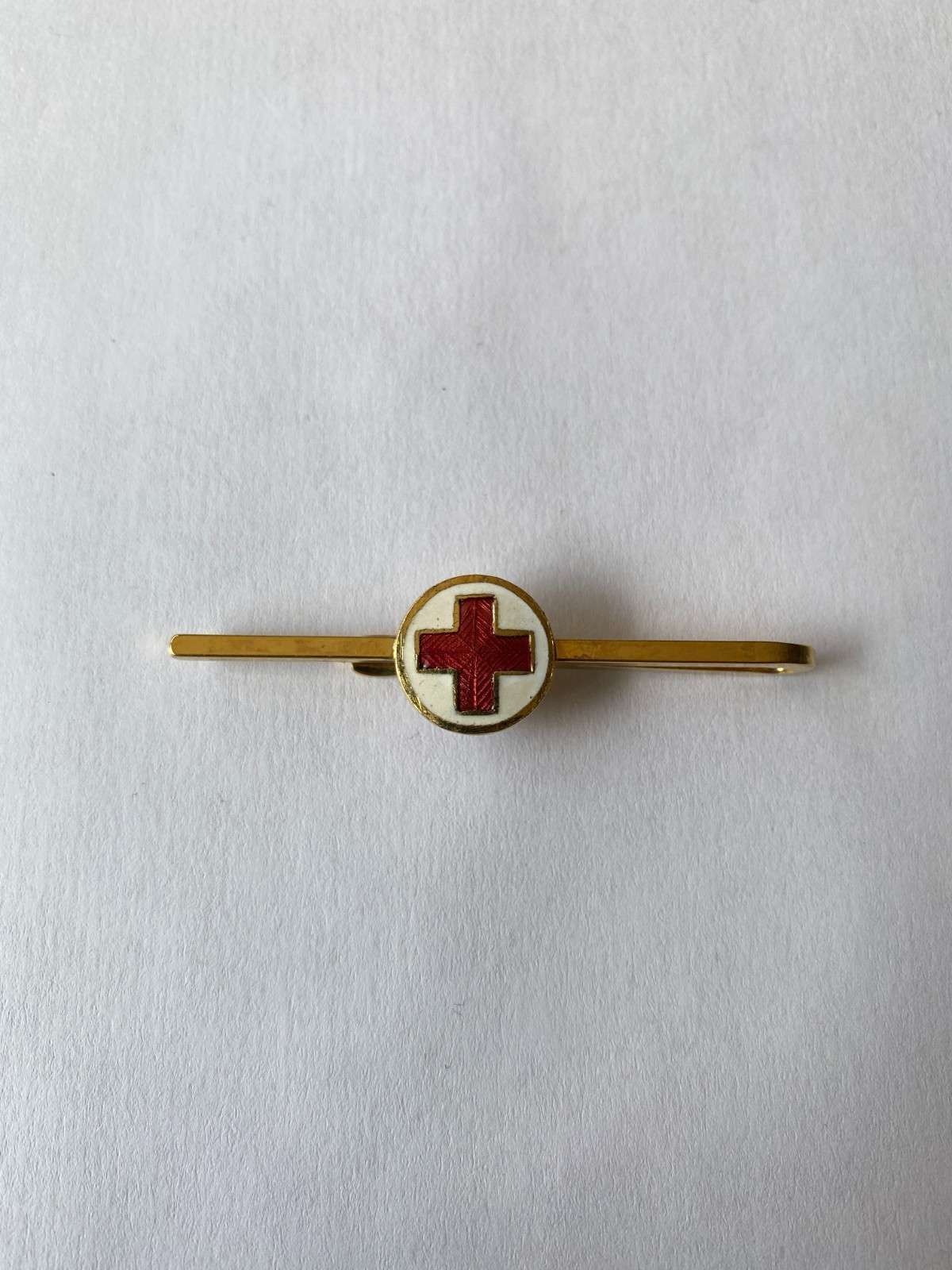 Pin dorado con emblema de cruz roja sobre fondo blanco